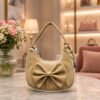 Cream-colored women’s sling bag with a large decorative bow, textured finish, and elegant gold-tone hardware.